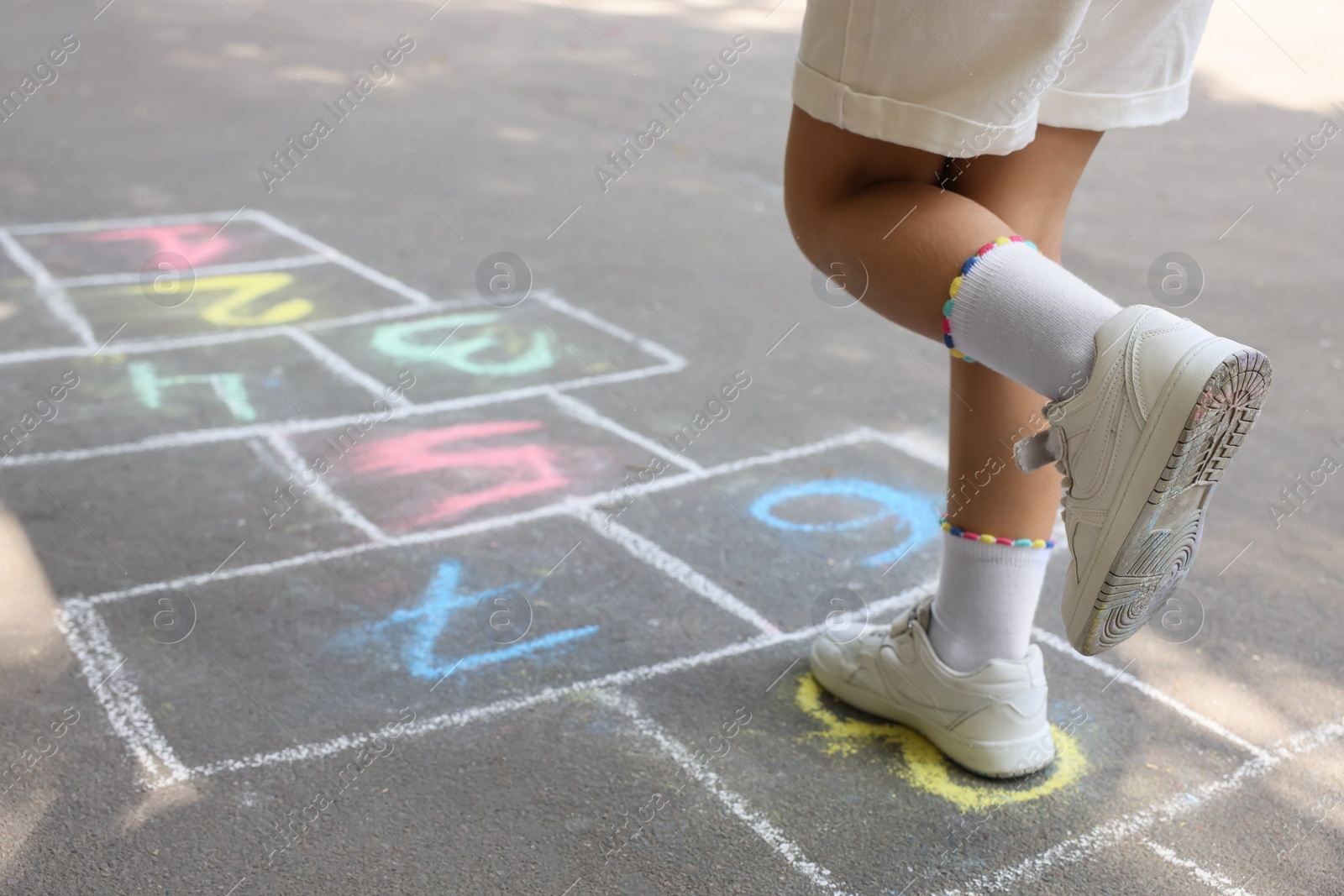 Photo of Little child playing hopscotch drawn with chalk on asphalt outdoors, closeup