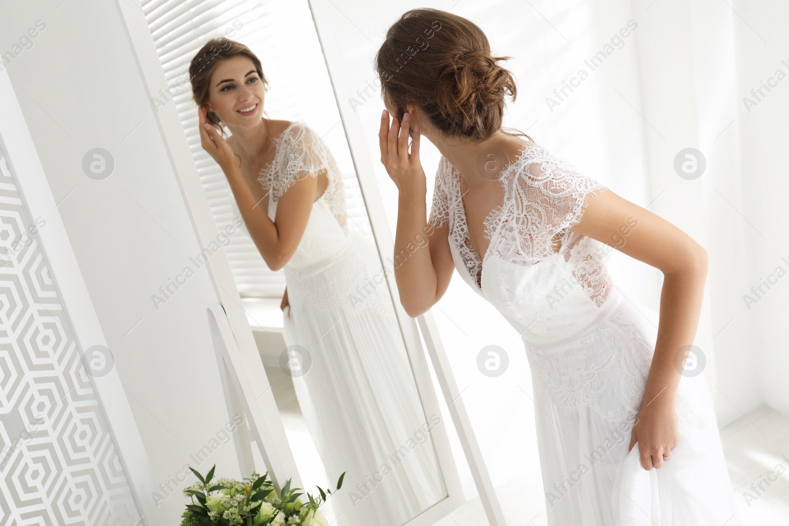 Photo of Young bride in beautiful wedding dress near mirror indoors