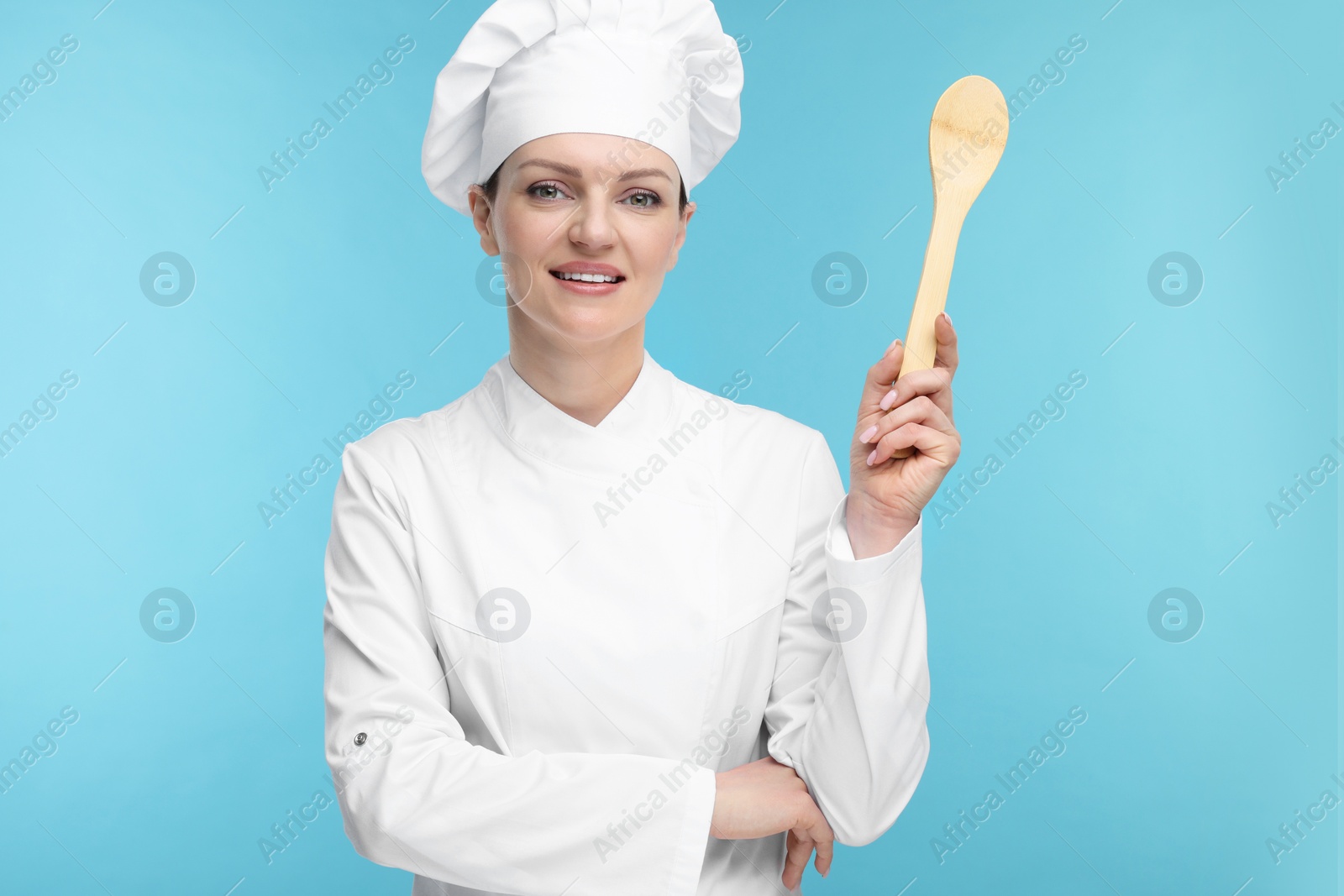 Photo of Happy woman chef in uniform holding wooden spoon on light blue background