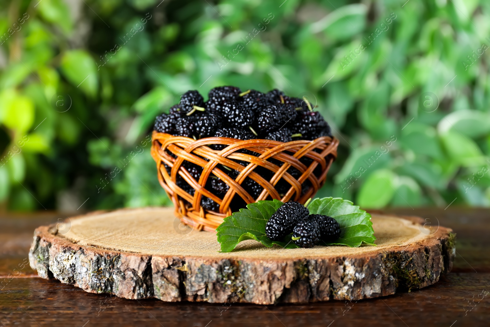 Photo of Fresh ripe black mulberries on wooden table against blurred background