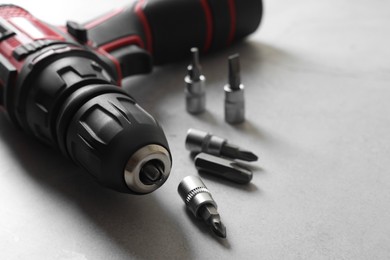 Photo of Modern electric screwdriver and bits on grey table, closeup. Space for text