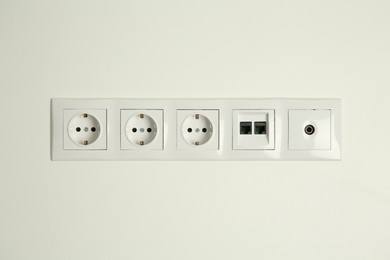 Many power sockets with ethernet and TV coax plates on white wall indoors