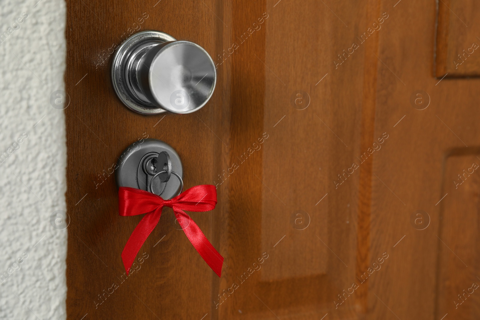 Photo of House key with red bow in door lock, closeup. Housewarming party