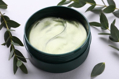 Photo of Under eye patches in jar near green twigs on white background, closeup. Cosmetic product