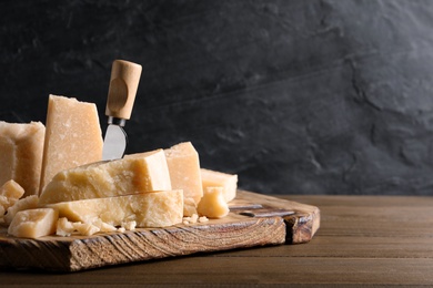 Photo of Pieces of delicious parmesan cheese with knife on wooden table. Space for text