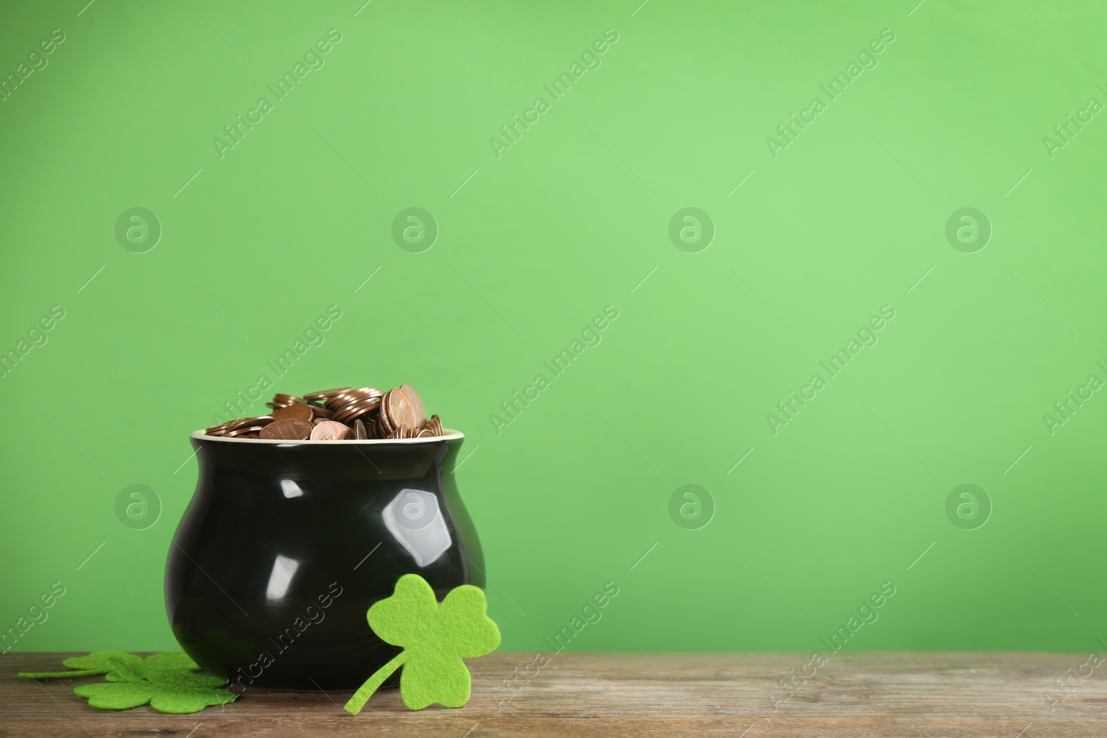 Photo of Pot of gold coins and clover leaves on wooden table against green background, space for text. St. Patrick's Day celebration