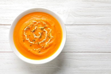 Photo of Bowl of tasty pumpkin soup and space for text on wooden table, top view