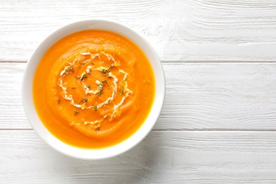 Bowl of tasty pumpkin soup and space for text on wooden table, top view