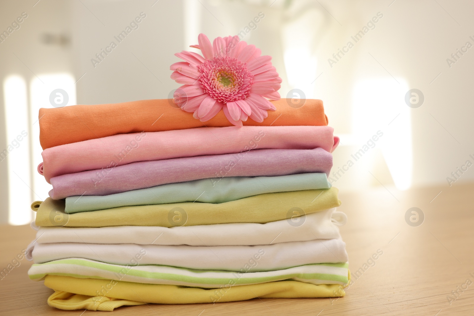 Photo of Stack of clean clothes and pink flower on wooden table