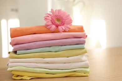 Photo of Stack of clean clothes and pink flower on wooden table