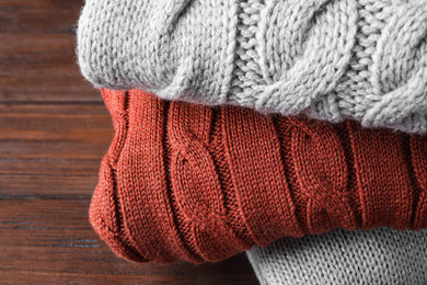 Image of Stack of folded warm sweaters on wooden background, closeup