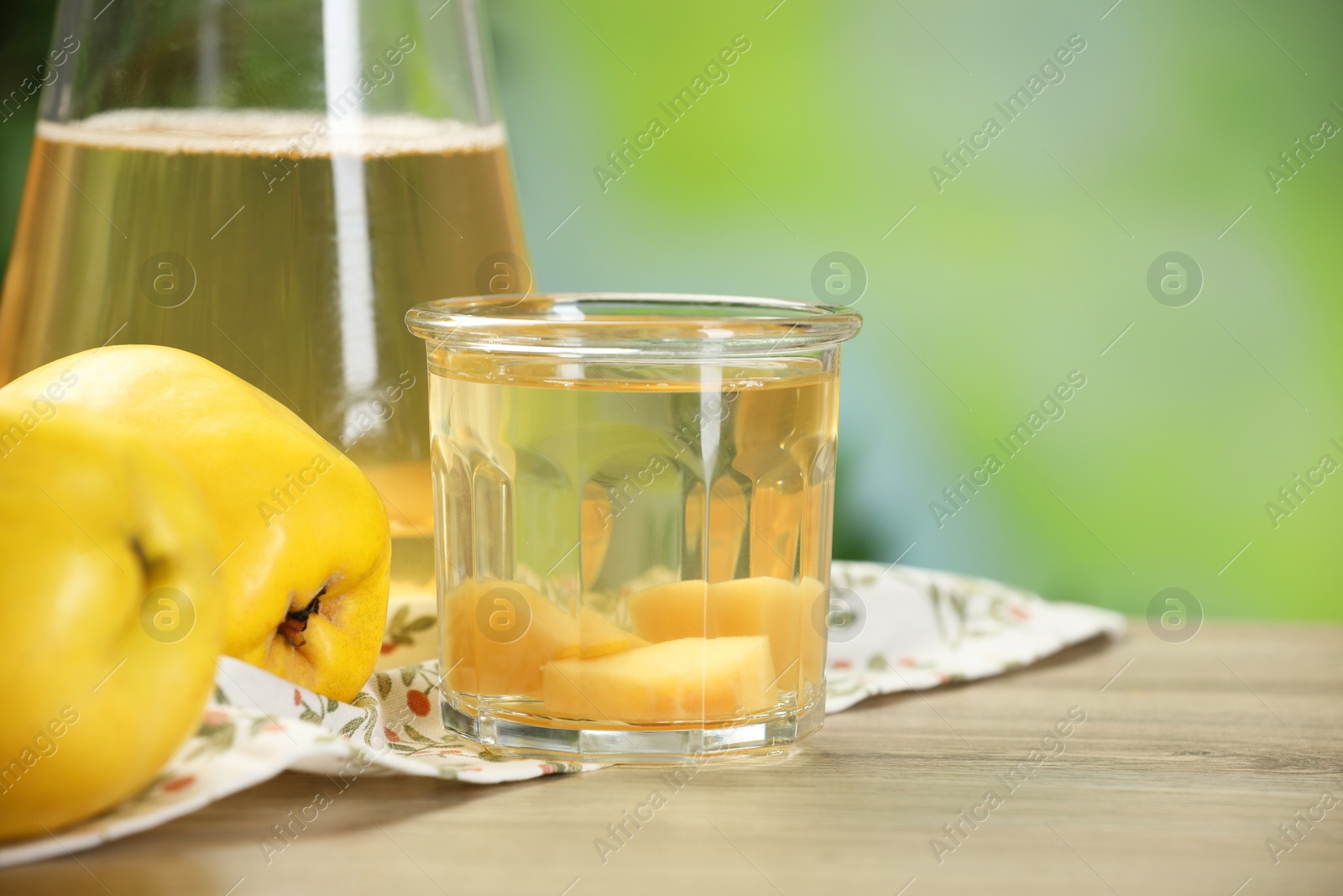 Photo of Delicious quince drink and fresh fruits on wooden table against blurred background, closeup