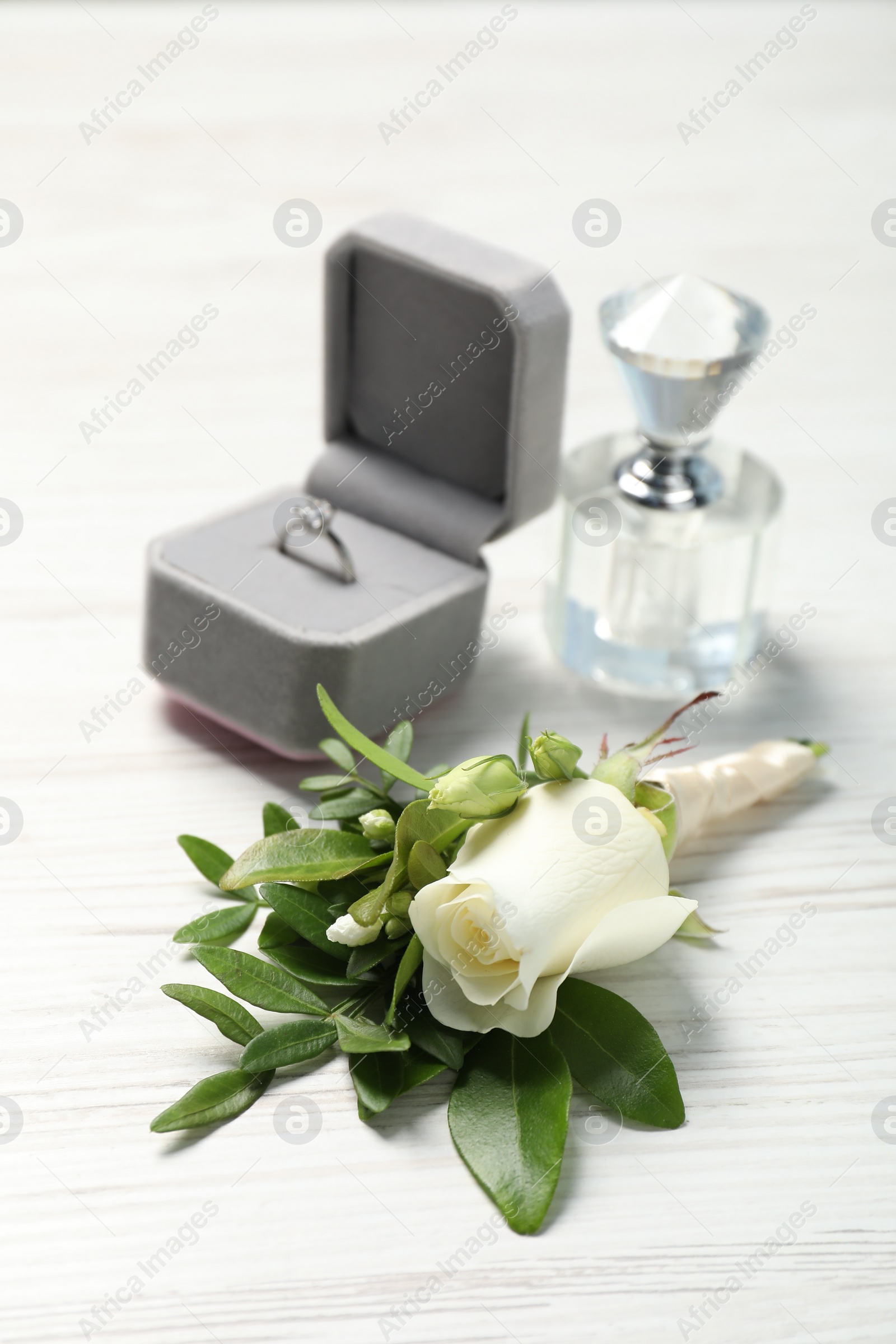 Photo of Wedding stuff. Stylish boutonniere, perfume and ring on white wooden table, closeup