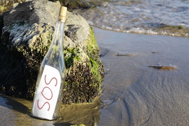 Glass bottle with SOS message near sea rocks, space for text