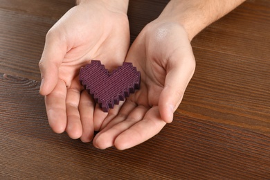 Photo of Man holding decorative heart on wooden background, closeup