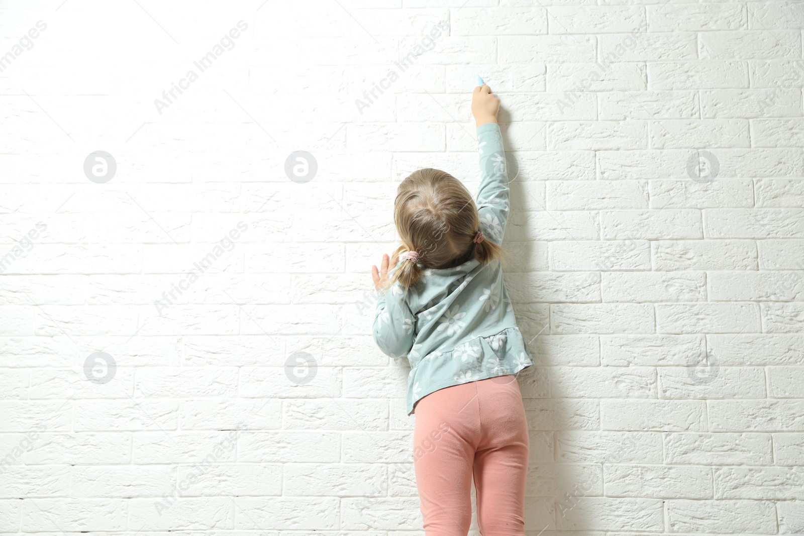 Photo of Little girl drawing on white brick wall, back view and space for text. Child`s art