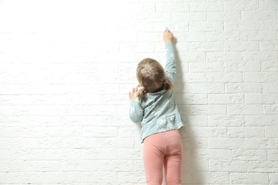 Little girl drawing on white brick wall, back view and space for text. Child`s art