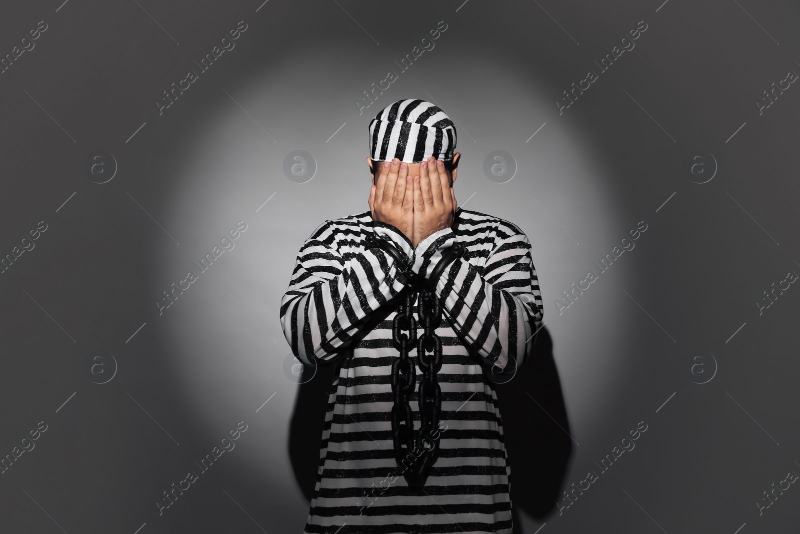 Photo of Prisoner in special uniform with chained hands on grey background