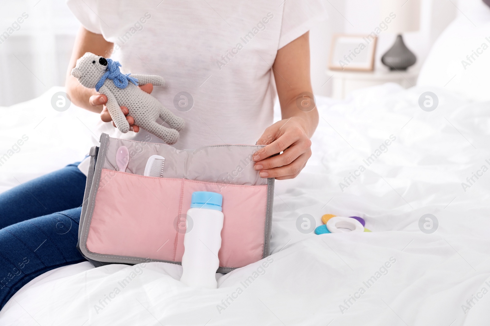 Photo of Woman packing baby accessories into maternity bag on bed, closeup