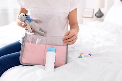 Woman packing baby accessories into maternity bag on bed, closeup