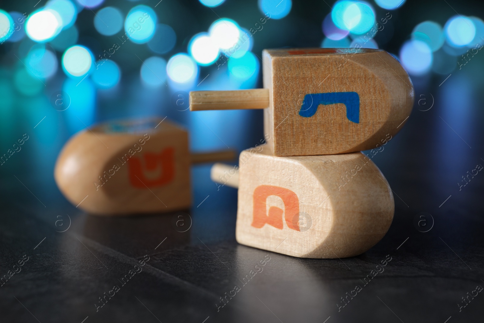 Photo of Hanukkah traditional dreidels with letters Nun and Shin against on table blurred lights, closeup