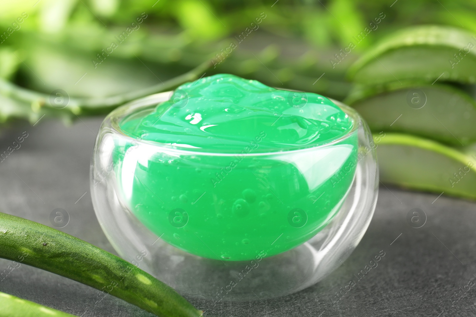 Photo of Bowl with natural gel and aloe vera leaves on dark grey table, closeup