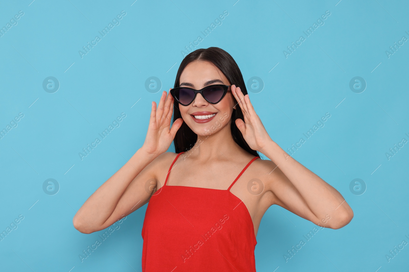 Photo of Attractive happy woman touching fashionable sunglasses against light blue background