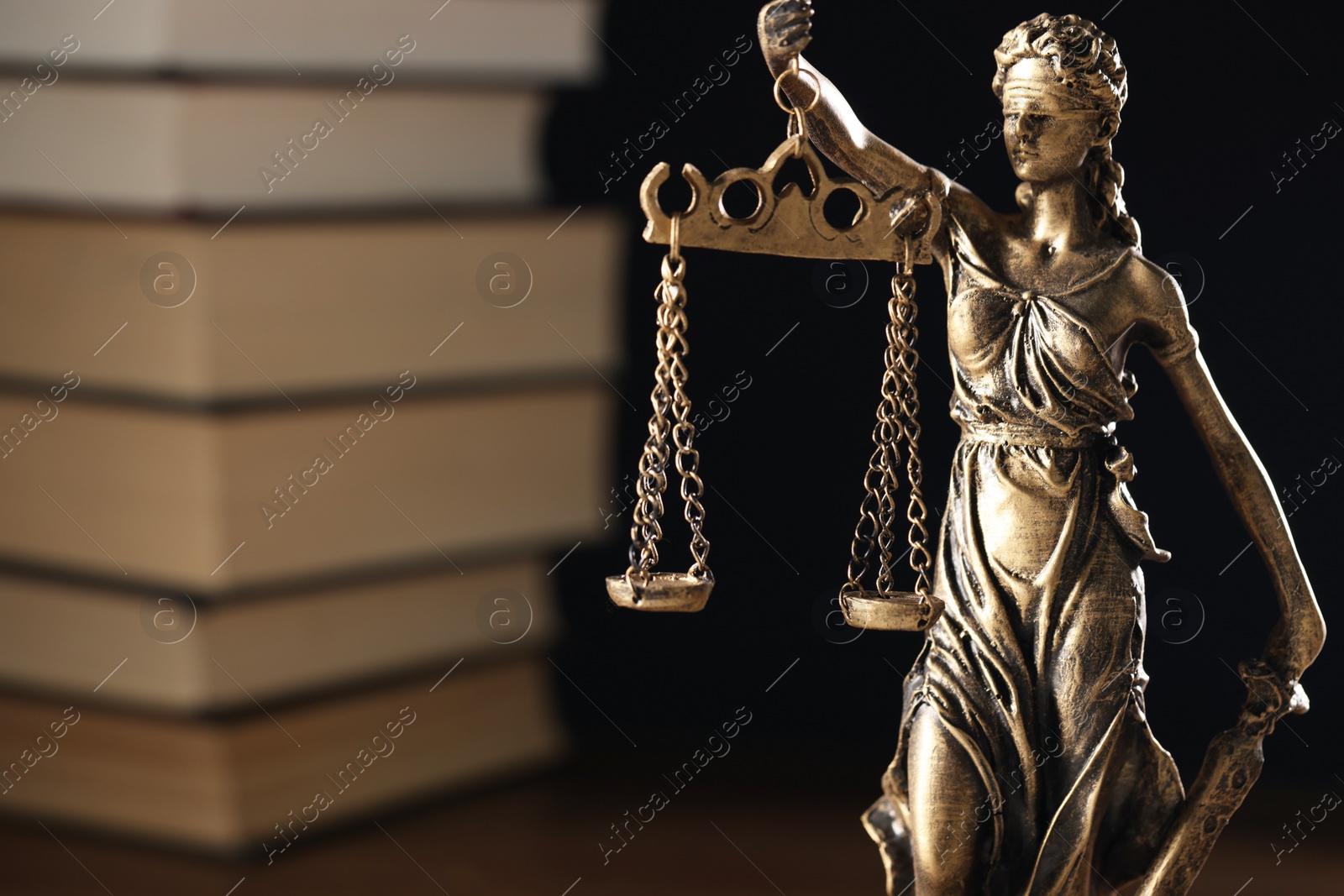 Photo of Symbol of fair treatment under law. Statue of Lady Justice near books on dark background, space for text