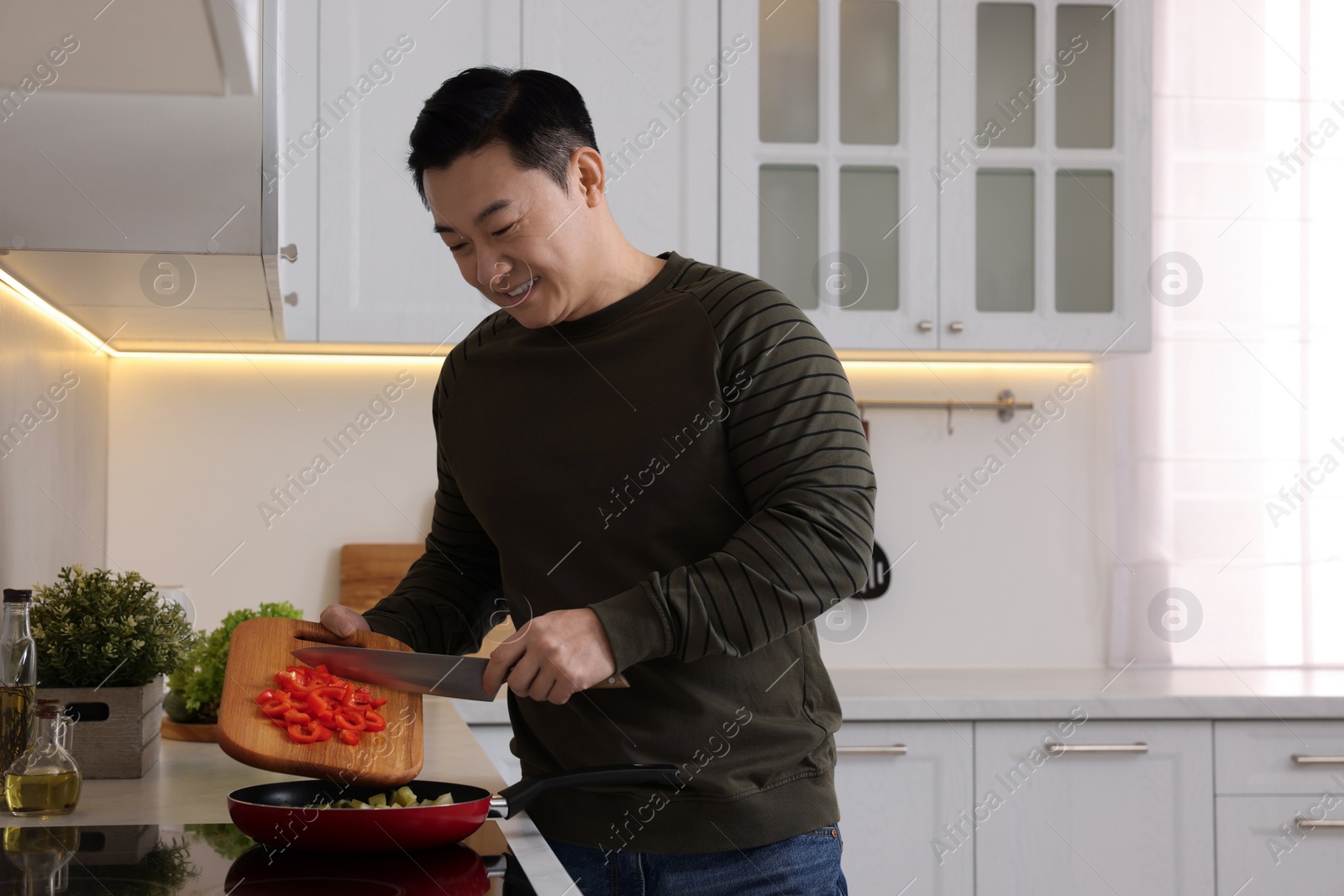Photo of Cooking process. Man adding cut bell pepper into frying pan in kitchen, space for text