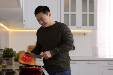 Cooking process. Man adding cut bell pepper into frying pan in kitchen, space for text