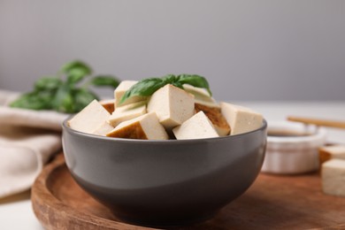 Photo of Bowl of smoked tofu cubes and basil on wooden tray, closeup