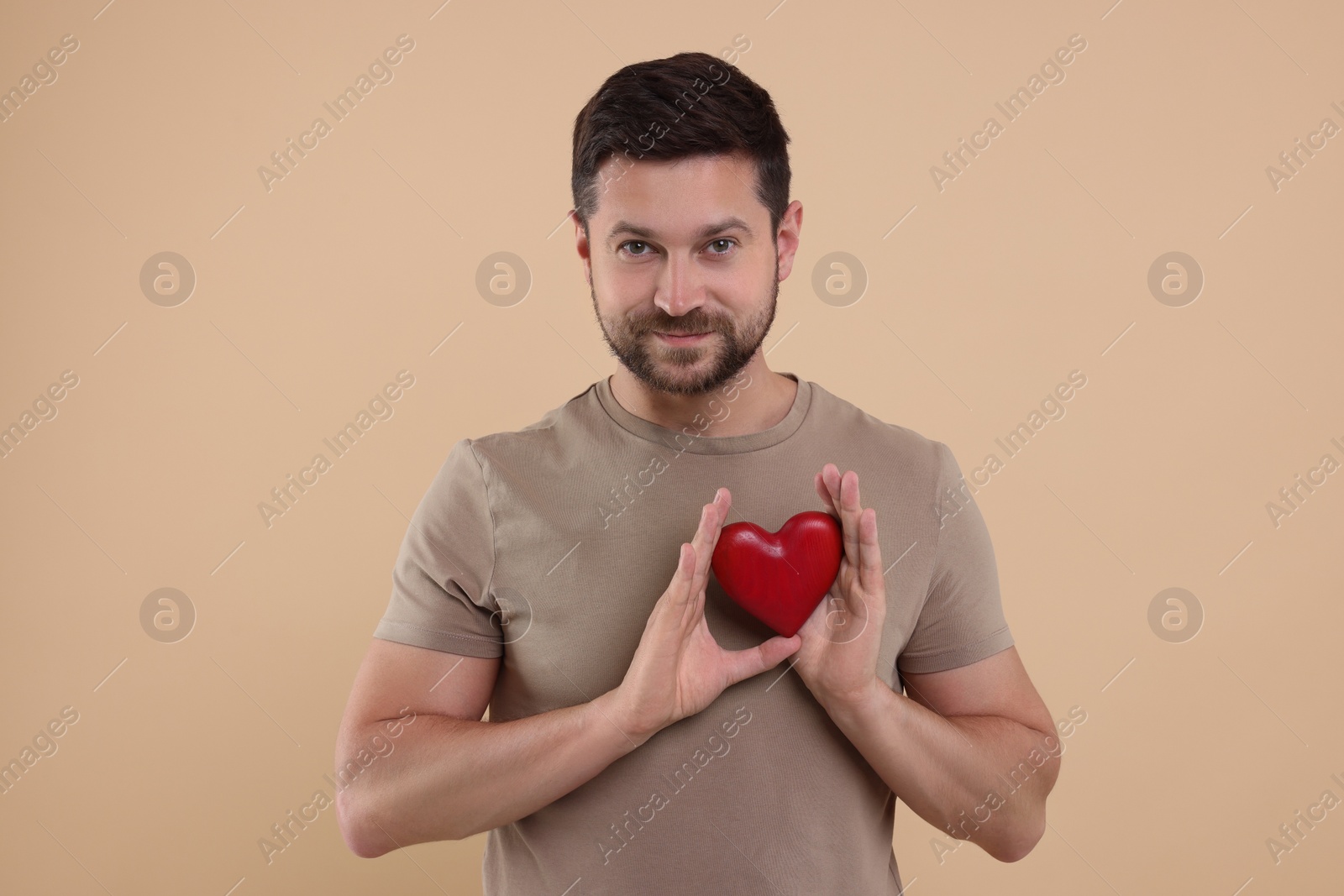 Photo of Happy man holding red heart on beige background