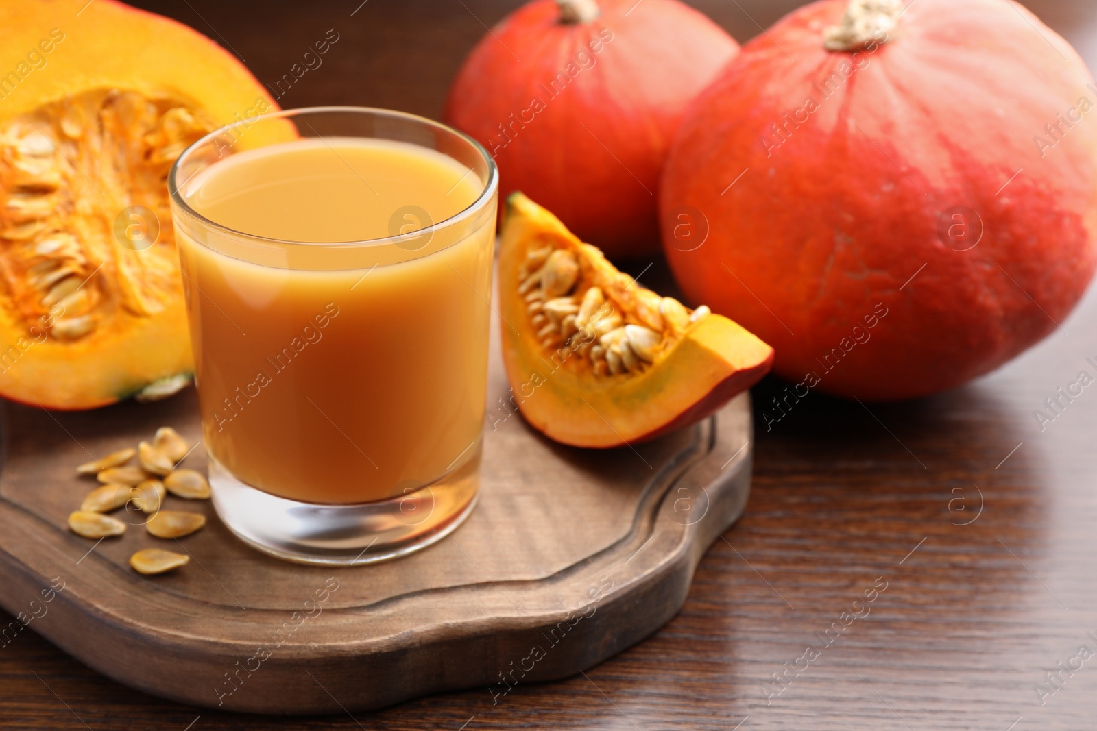 Photo of Tasty pumpkin juice in glass, whole and cut pumpkins on wooden table. Space for text