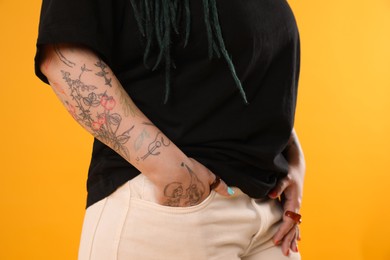 Young woman with tattoos on arm against yellow background, closeup