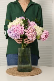 Photo of Woman with beautiful hydrangea flowers at table indoors, closeup. Interior design element