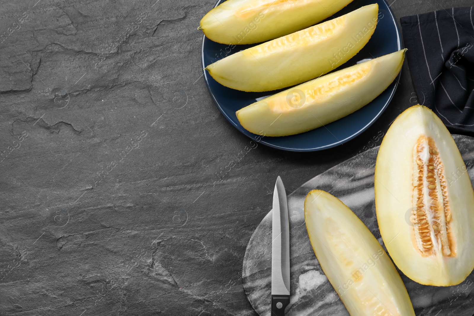 Photo of Pieces of delicious honeydew melon on black slate table, flat lay. Space for text