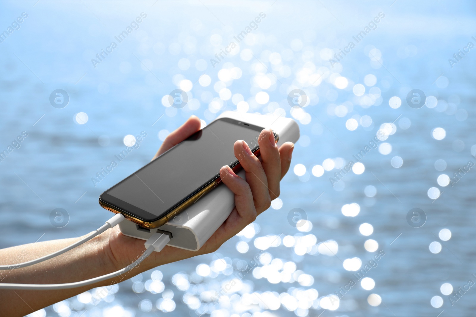 Photo of Woman charging smartphone with power bank on rocky mountain near river, closeup