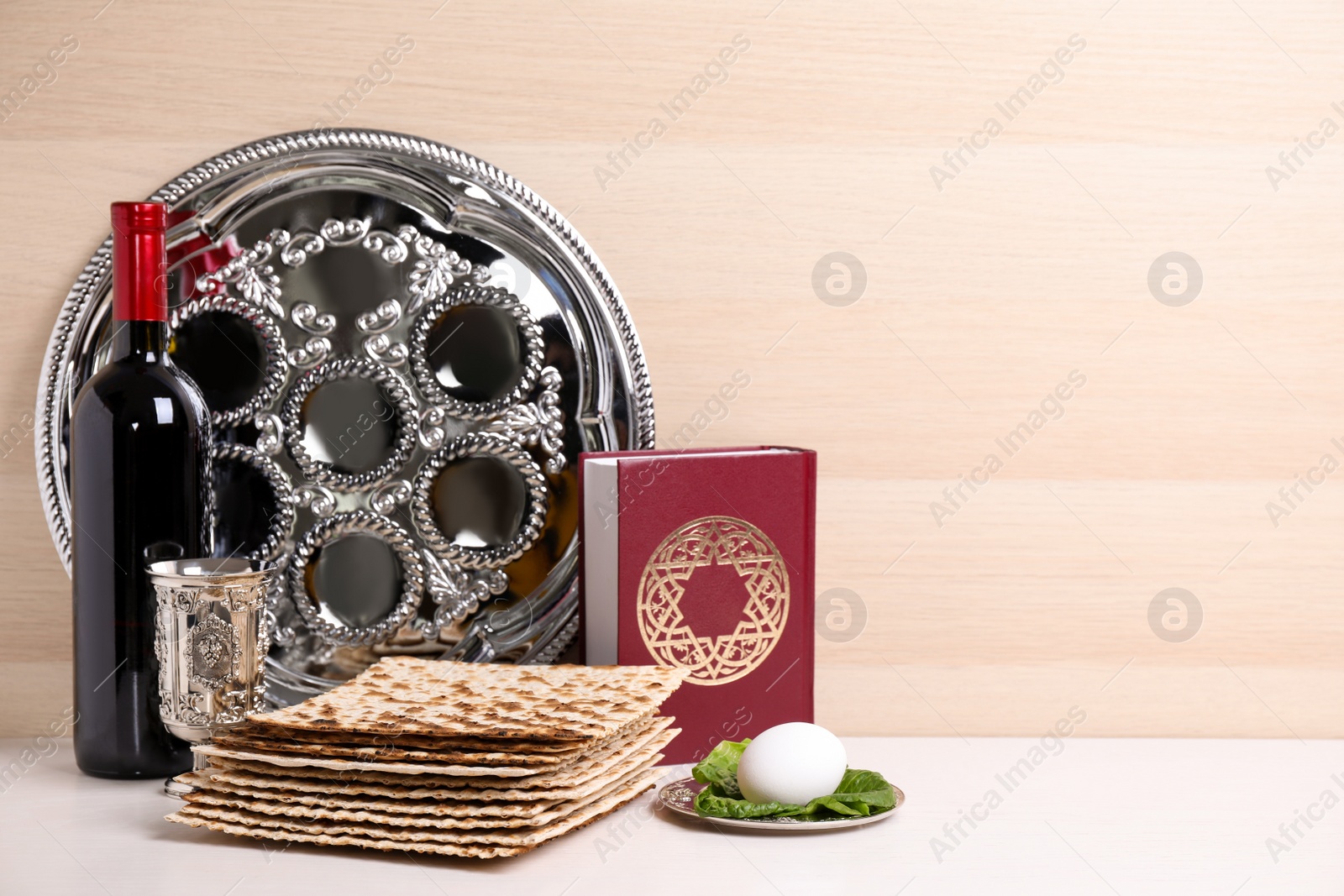 Photo of Symbolic Pesach (Passover Seder) items on white table against wooden background, space for text