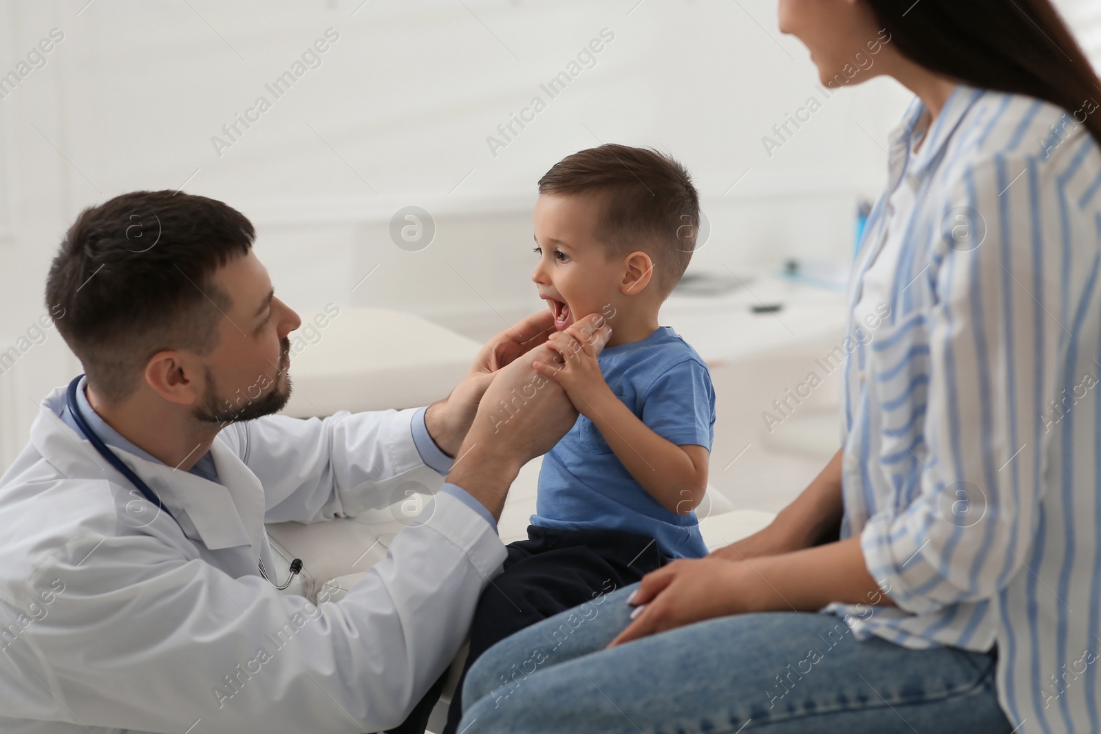 Photo of Mother and son visiting pediatrician in hospital. Doctor examining little boy