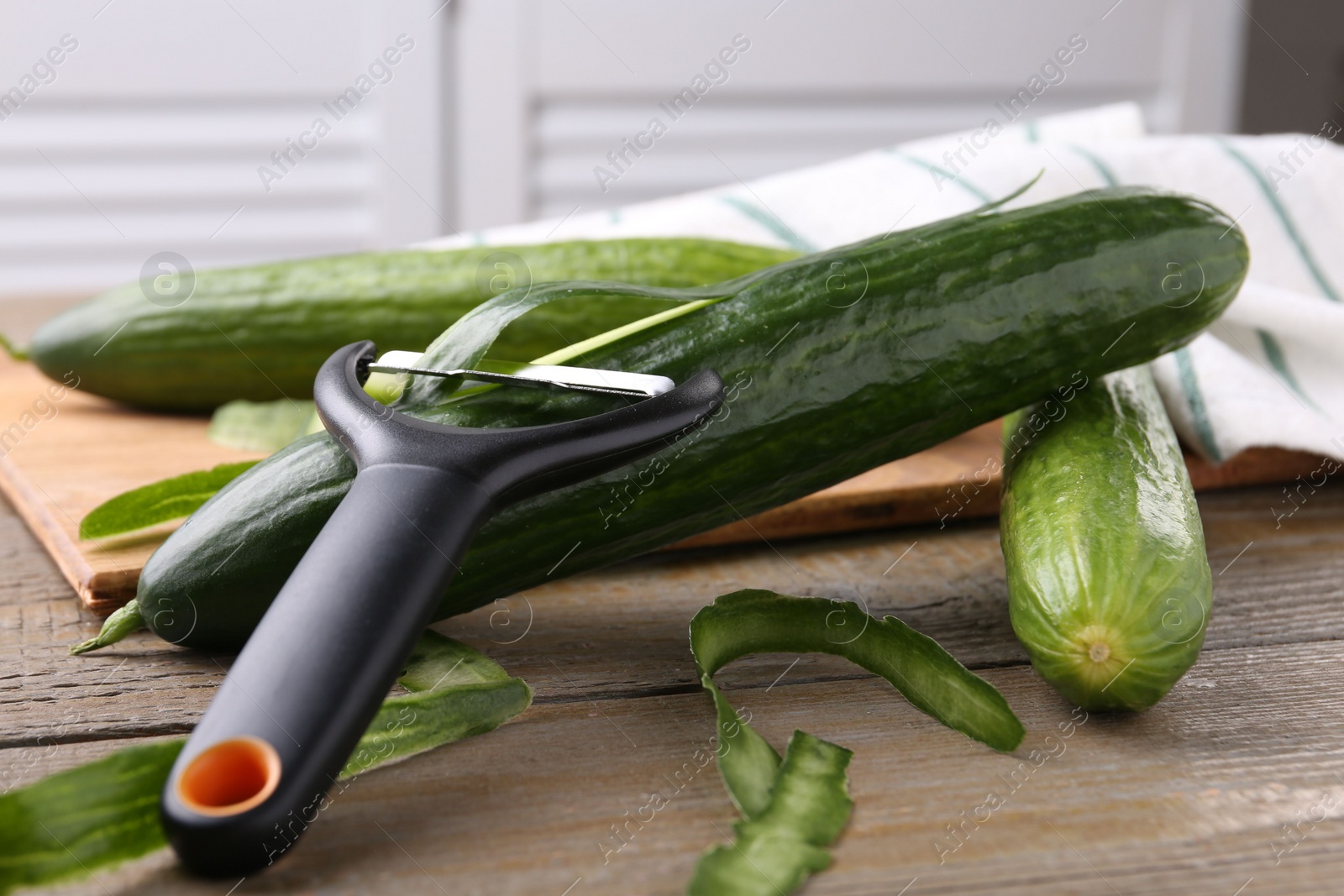 Photo of Fresh cucumbers, peels and peeler on wooden table, closeup