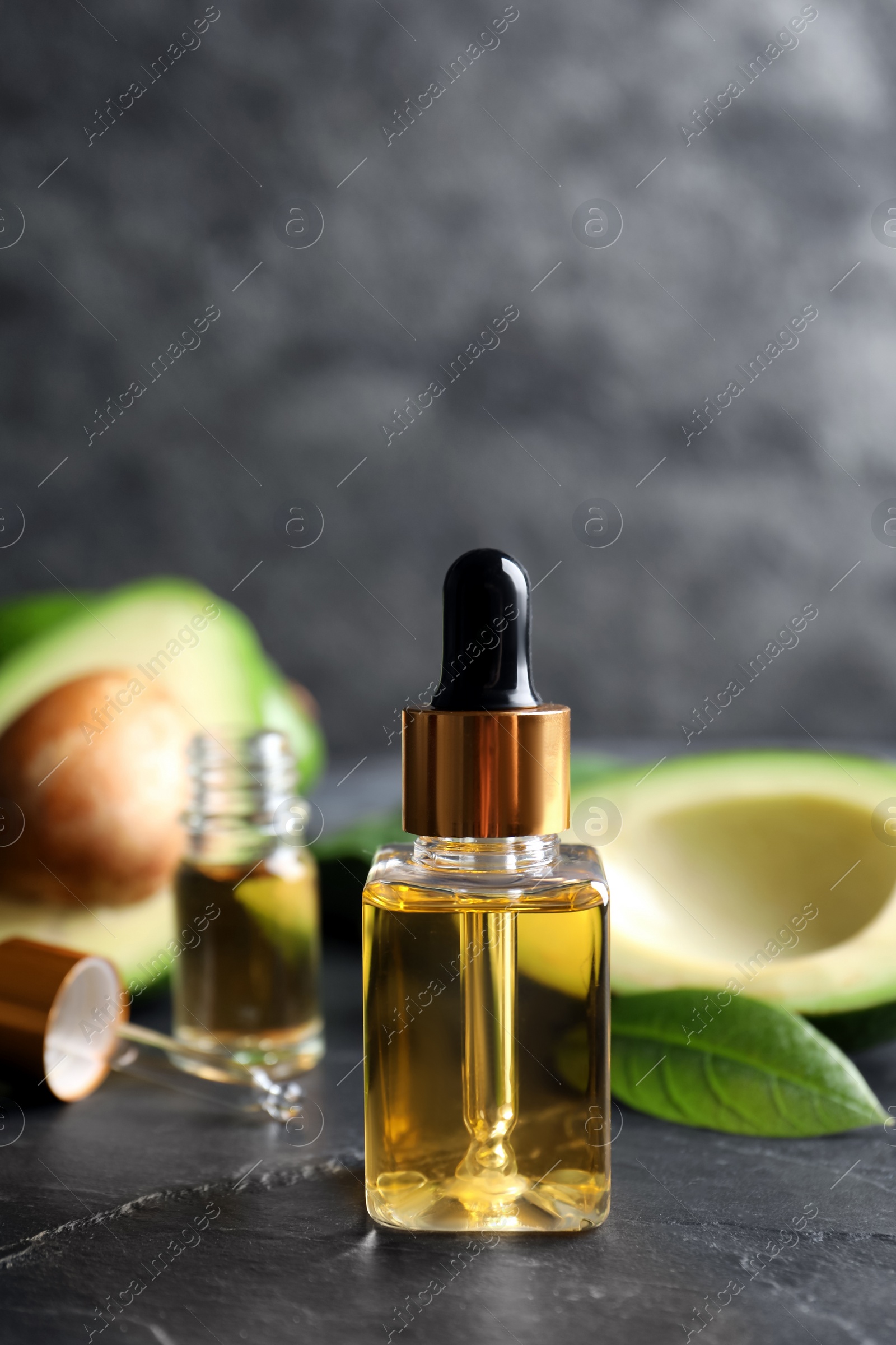 Photo of Bottle of essential oil and fresh avocado on black table