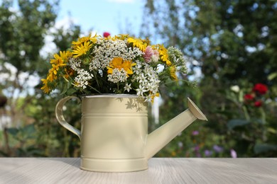 Photo of Beautiful bouquet of bright wildflowers in watering can on white wooden table outdoors