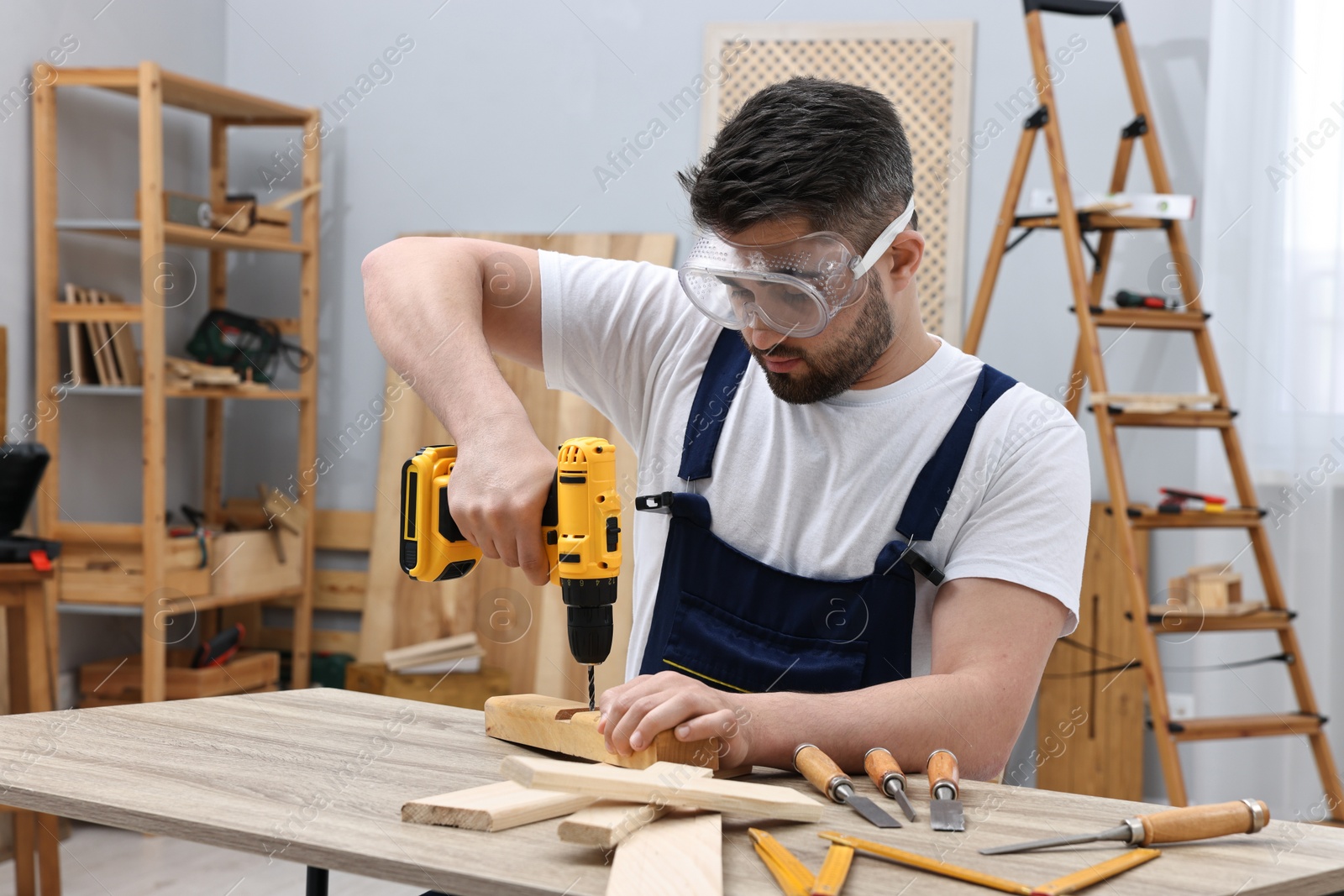 Photo of Young worker using electric drill at table in workshop