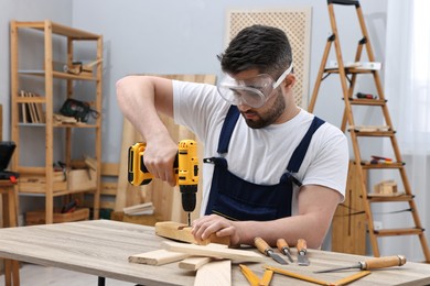 Young worker using electric drill at table in workshop