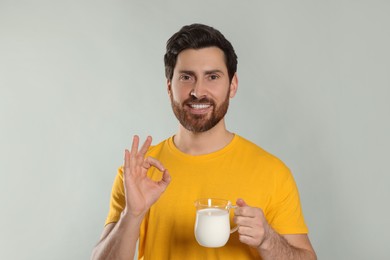Photo of Handsome man with delicious yogurt showing ok gesture on light grey background
