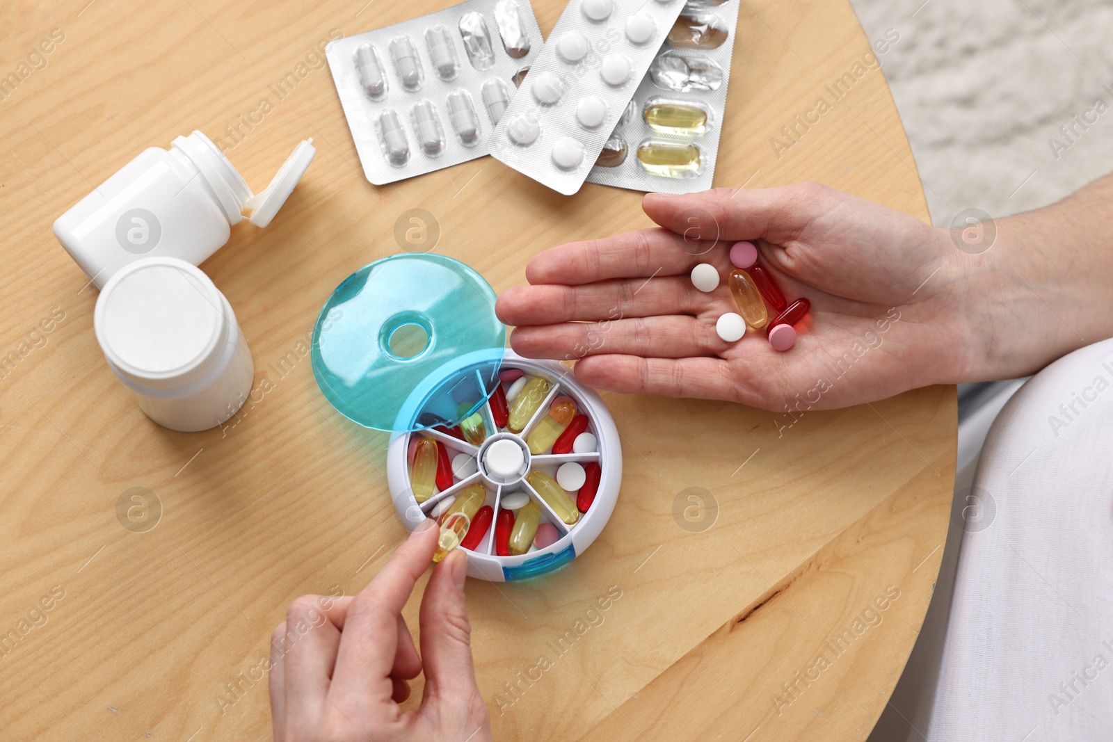 Photo of Woman with pills and organizer at light wooden table, closeup