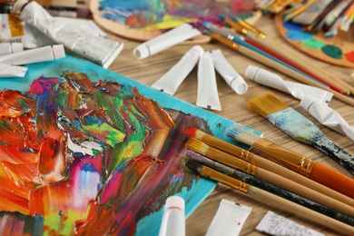 Photo of Set of different brushes, paints and abstract picture on wooden table, closeup