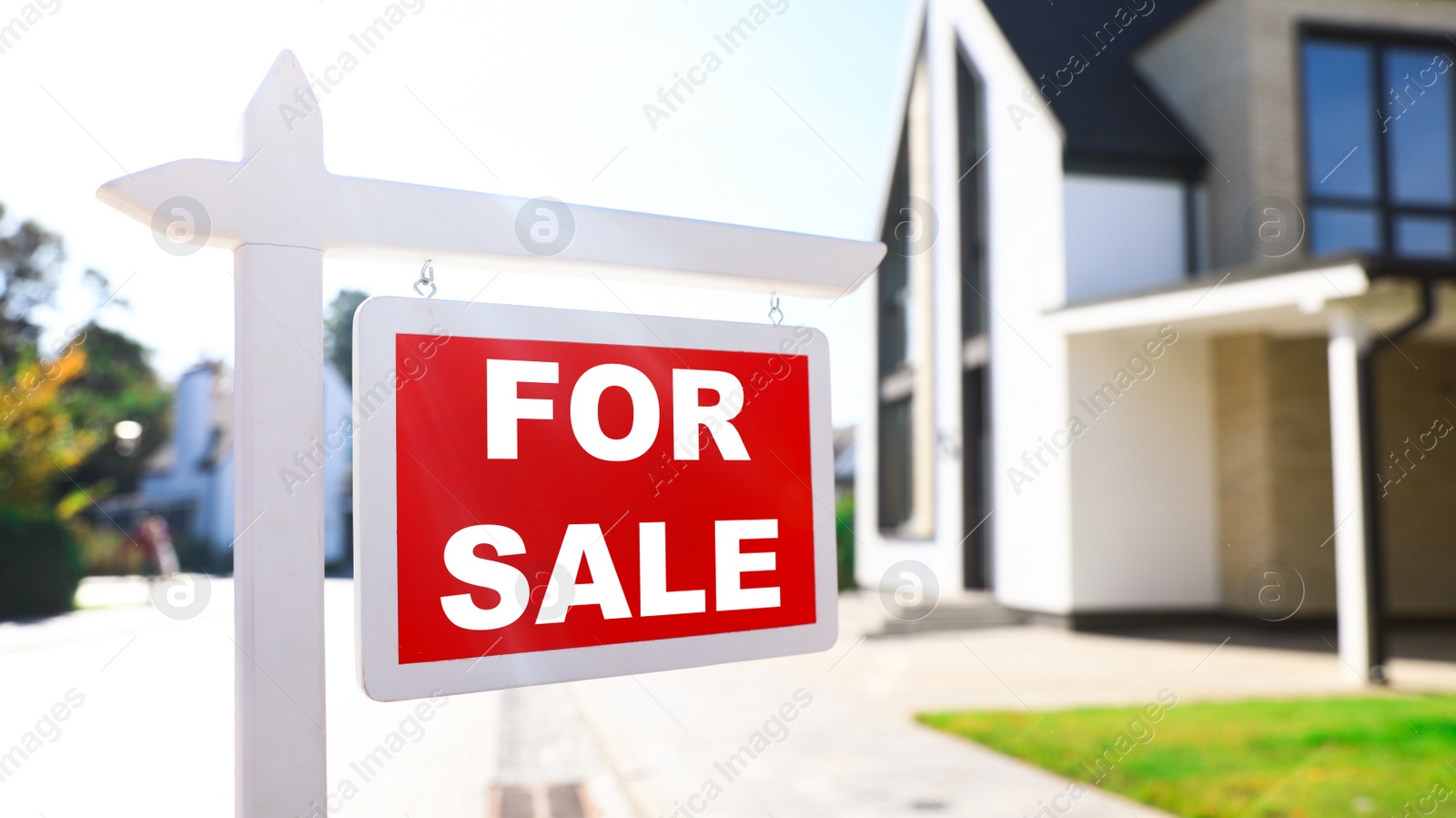 Photo of Red real estate sign near house outdoors on sunny day