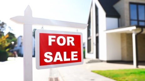 Photo of Red real estate sign near house outdoors on sunny day