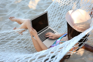 Photo of Young woman with laptop resting in hammock at seaside. Summer vacation